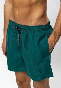 Zaļie peldkostīmi, izgatavoti no gludas, vieglas auduma. Iespējas ar elastīgu jostu ar auklu un sānu kabatām. Mazs logotipa elements.