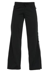 Pantalones deportivos negros con un corte relajado, cinturilla elástica y cordón. Presentan texto blanco y un detalle de franjas en el lateral. Textura de tejido suave.