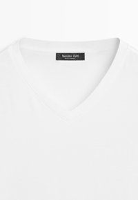 T-shirt blanc à col en V avec une étiquette noire visible portant l'inscription "Massimo Dutti Made in Portugal" à l'intérieur du col arrière.
