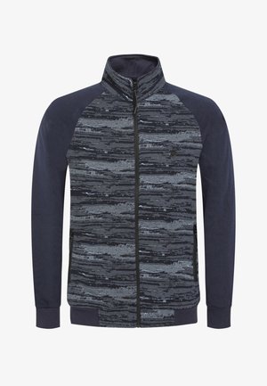 Chaqueta con cremallera que presenta una parte superior de gris y negro con un diseño, mangas azul oscuro y puños sólidos. Textura suave con bolsillos laterales.