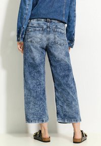 Wijdvallende, lichtblauwe denim broek met een vervaagde wassing, vijf zakken en een rechte zoom. Gestyled met zwarte instapsandalen.