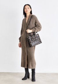 Brun strikket cardigan med v-hals, lange ærmer og knapper. Sort håndtaske med guldmønstre og metalaccenter. Knæhøje sorte støvler.