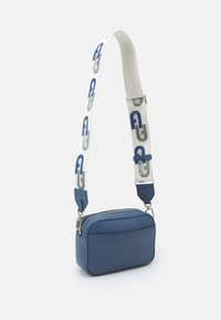 Blå läder crossbody-väska med dragkedjestängning, med en justerbar rem med gröna och blå mönster, och rundade kanter.