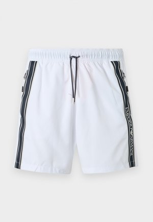 Valged ujumispüksid musta paelaga, mustad küljetriibud tekstiga „EMPORIO ARMANI“ ja lukuga taskud mõlemal küljel.