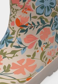 Κοντινό πλάνο μιας μπότες με πολύχρωμο λουλουδάτο σχέδιο σε μπλε, κοραλί, πορτοκαλί και πράσινο σε μπεζ φόντο.