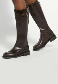 Brown leather knee-high boots with a sleek design, featuring a side zipper and a buckle accent on the cuff. Flat sole with a slight heel.
