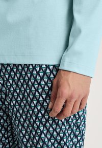  Lichtblauwe lange mouwen top gecombineerd met een patroon van donkere stof met witte en teal geometrische vormen, een gladde textuur en een getailleerd ontwerp.