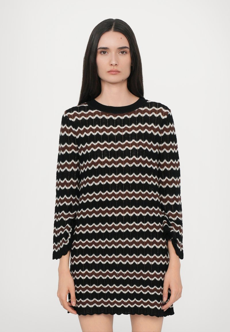 Robe noire en tricot avec un motif en zigzag crème et marron, manches longues, encolure ronde et ourlet à bords festonnés. Matière texturée.