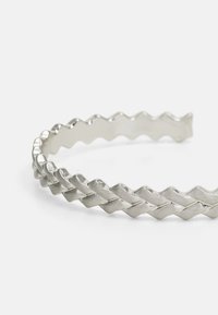 Bracelet en argent tissé avec un motif en zigzag, texture lisse et design ouvert pour un ajustement réglable.