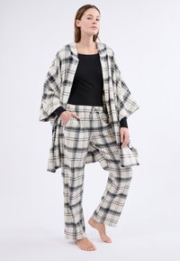 Ensemble de loungewear à carreaux comprenant un haut noir ample et un pantalon à carreaux beige et noir assorti, doté d'une taille élastique et de poches.