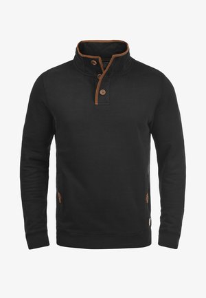 Hanorac negru cu guler înalt și trei butoane maronii. Prezintă accente maronii în jurul gulerului și la buzunarele laterale. Fabricat dintr-un material moale.