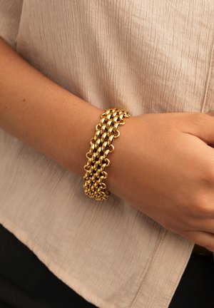 Goldfarbene Kettenarmband mit ineinander verlinkten runden und ovalen Gliedern. Glatte Textur mit polierter Oberfläche. Am Handgelenk getragen.