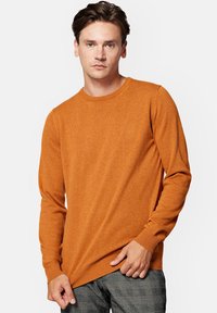 Pomarańczowy sweter dziewiarski z długimi rękawami, okrągłym dekoltem i ściągaczem u dołu. Posiada małe logo na klatce piersiowej. Gładki, teksturowany materiał.