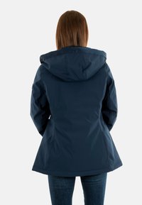 Giacca impermeabile blu navy con cappuccio, caratterizzata da una silhouette aderente e una consistenza liscia. I dettagli includono un design delle cuciture sottile.