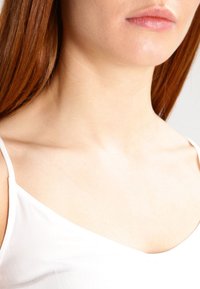 Mujer con largo cabello rojo que lleva una blusa blanca de tirantes, mostrando el cuello, la clavícula y los labios.
