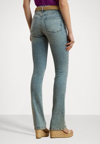 Falmede blå denimjeans med en tettsittende fasong, to baklommer og et flettet belte i lys brun, kombinert med kilehælsandaler.