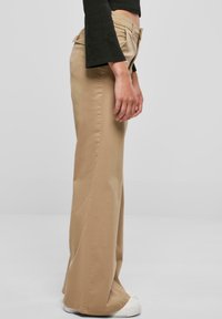 Lichtbeige pantalons met een aansluitende taille, uitlopende pijpen en een effen stof. Voorzien van zakken aan de voorkant, een knoopsluiting en een gladde textuur.