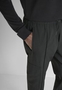 Donker gekleurde joggers van stof met een elastische tailleband, zijzakken en een zichtbare cargozak op het been. Zachte textuur en een getailleerde pasvorm.