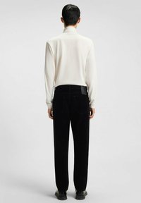 Camicia bianca a maniche lunghe abbinata a pantaloni in corduroy neri. La camicia è liscia; i pantaloni hanno una finitura testurizzata con una vestibilità dritta e tasche visibili.