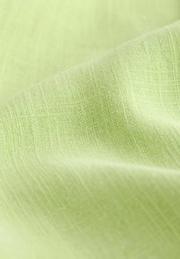 Tissu vert clair avec une surface douce et texturée. Le matériau présente un motif de tissage subtil, créant une apparence délicate et aérienne.