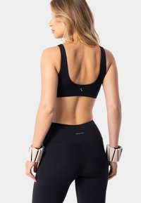 Sujetador deportivo negro con un respaldo ancho, combinado con mallas negras de cintura alta. Pesas de muñeca de colores claros notables. Textura de tela suave.