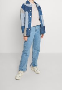 Jeansjacka i patchwork i blå nyanser, beige sweatshirt med rund hals och logotyp, ljusblå raka jeans och beiga sneakers.