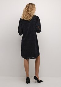 Abito nero a fiori realizzato in materiale trasparente con maniche a palloncino, l'orlo arriva a metà coscia, abbinato a scarpe nere con tacco alto.