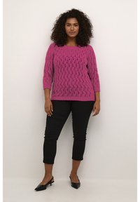 Maglione rosa lavorato a maglia con motivo a onde e maniche tre quarti, abbinato a pantaloni neri a 3/4 e scarpe nere con punta.