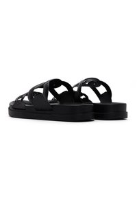 Sandalias negras con un acabado texturizado, que presentan correas entrecruzadas y un diseño de suela plana. Forma minimalista sin acentos adicionales.