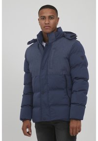 Navy blue puffer jacket with a blended fabric upper, high collar, zip pockets, and buttons, featuring a hood with adjustable toggles.