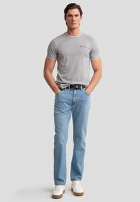 Camiseta de algodón gris con cuello redondo, combinada con jeans de mezclilla azul claros y zapatillas blancas. Cinturón negro incluido. Diseño simple.