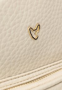 Borsa in pelle crema con logo in rilievo dorato, superficie testurizzata e cuciture di alta qualità, dettagli con zip lungo il bordo inferiore.
