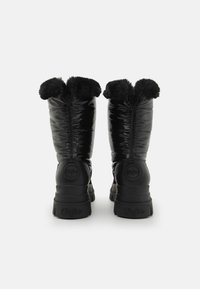 Botas de estilo plumas negras con un acabado brillante, un lujoso cuello de pelo sintético negro y una suela de goma gruesa con un detalle de logo en la parte posterior.