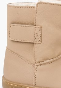 Beżowy botek ze skóry z miękkim wnętrzem, wyposażony w pasek na rzep oraz ozdobne przeszycia wzdłuż szwów. Podeszwa z formowanej gumy.
