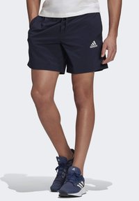 Pantalones cortos deportivos de color azul marino, confeccionados con tela ligera, que cuentan con una banda elástica en la cintura con cordón y un logo blanco de Adidas en el lado izquierdo.