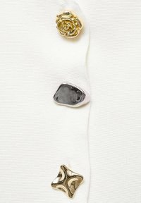 Quattro bottoni decorativi su un tessuto bianco: una rosa dorata, un argento scuro liscio, un ovale metallico texture e una forma a stella dorata lucente.