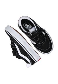 Zapatillas de lona negras con suelas de goma blancas, con tiras de velcro y costuras blancas a contraste, con un diseño clásico de corte bajo.