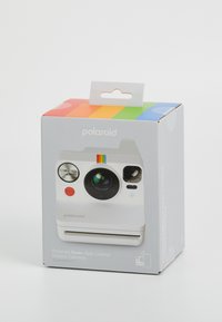 Boîte de l'appareil photo instantané Polaroid Now+ avec un design blanc, un objectif rond, un bouton rouge et une bande colorée en haut. Inclut des détails sur le contrôle via l'application.