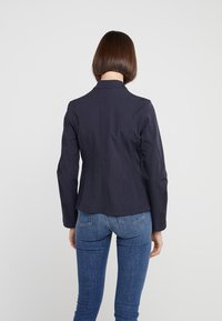 Navy fitted jacket with a notched collar and structured shoulders; smooth texture with subtle seams and a clean finish at the hem.