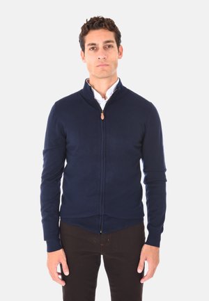 Cardigan blu navy con zip, realizzato in tessuto a maglia, con colletto alto, polsini a coste e un tirante in pelle sulla cerniera.
