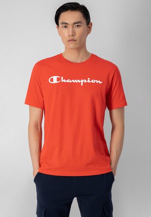 Crvena pamučna majica s kratkim rukavima, s velikim bijelim "Champion" logotipom na prsima. Dizajn s okruglim izrezom. Jednostavna tekstura tkanine.