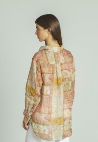 Camisa de manga larga, ligera, con un diseño de patchwork en colores pastel como rosa, amarillo y crema, que presenta patrones florales y ornamentales.