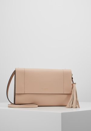 Beige leren crossbodytas met flapsluiting en zij-tassel, liggend op een witte ondergrond tegen een effen lichtgrijze achtergrond.