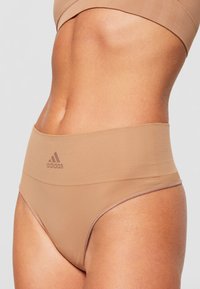 Hochtaillierte Unterwäsche in Beige mit glatter Textur, die ein Adidas-Logo in einem leicht dunkleren Farbton und dezente Details am elastischen Bund aufweist.