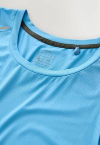 Jasnoniebieska koszulka sportowa z teksturowanej tkaniny o okrągłym dekolcie, z ciemnoszarym akcentem przy dekolcie oraz nadrukowanymi detalami logo.
