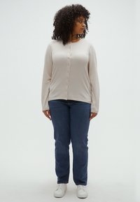 Beige long-sleeve cardigan with a button front, paired with blue straight-leg jeans and white sneakers. Simple design and soft texture.