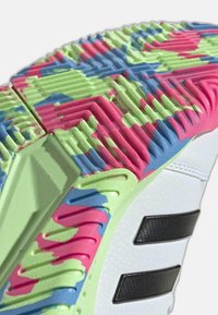 La semelle de la chaussure présente des motifs vibrants en rose, vert et bleu avec des rainures texturées. Les accents comprennent des rayures noires et une partie supérieure blanche.