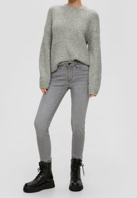 Pull en maille grise texturée avec épaules tombantes, assorti à un jean gris slim et des bottines noires à lacets avec une semelle plateforme.