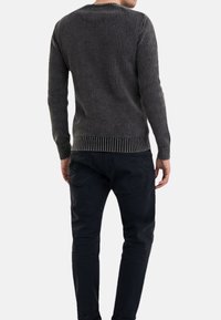 Maglione grigio a coste con maniche lunghe, scollatura rotonda e lavorazione a maglia testurizzata. Abbinato a jeans in denim scuro, mostra la vista posteriore e uno stile aderente.