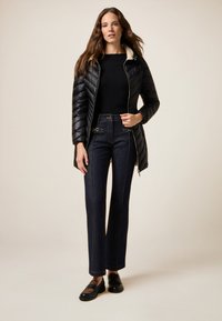 Chaqueta de plumas negra con un cuello crema, combinada con pantalones de mezclilla oscuros de tiro alto que presentan herrajes dorados. Mocasines negros con recortes a rayas.